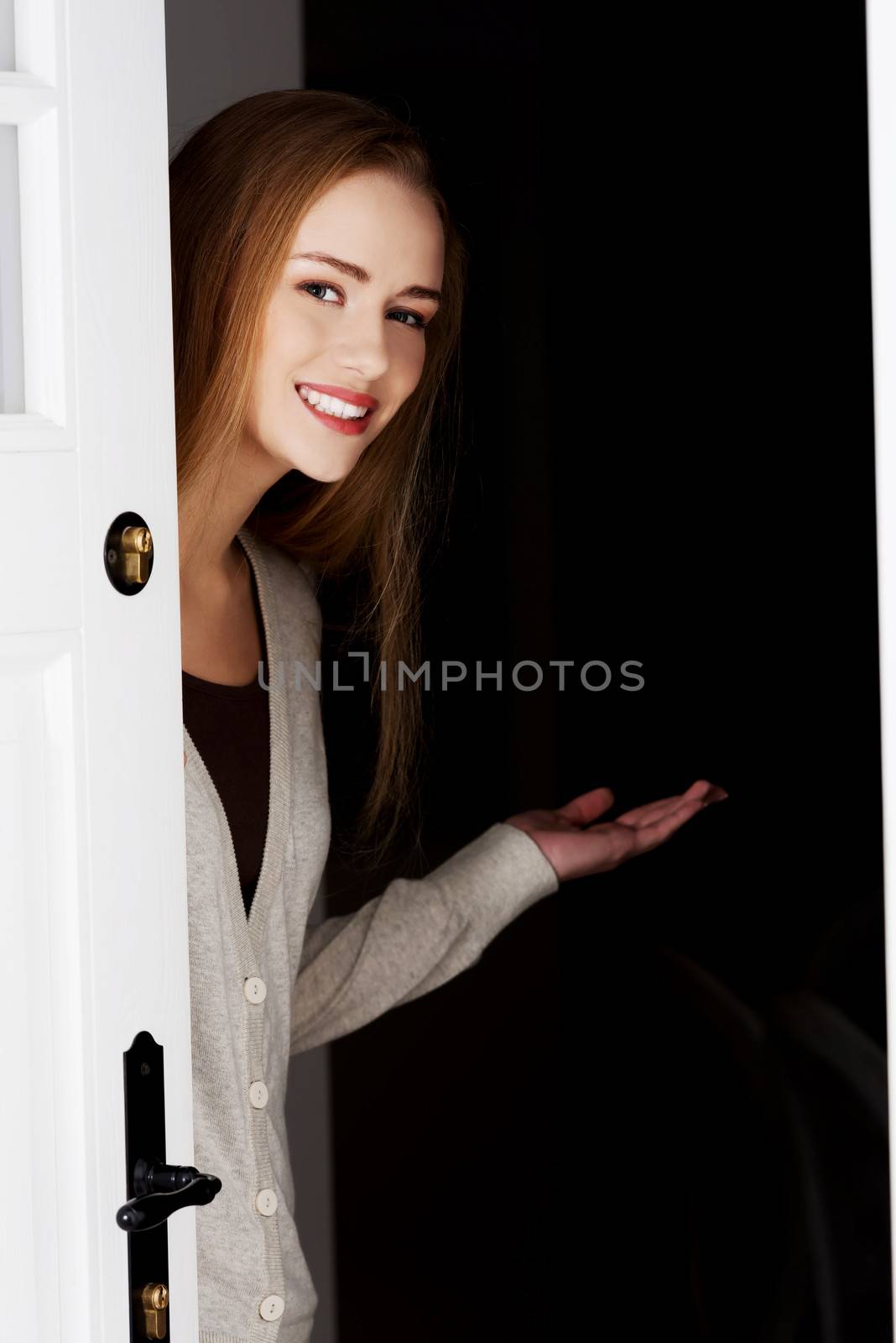 Beautiful smiling woman is opening door and inviting to come in.