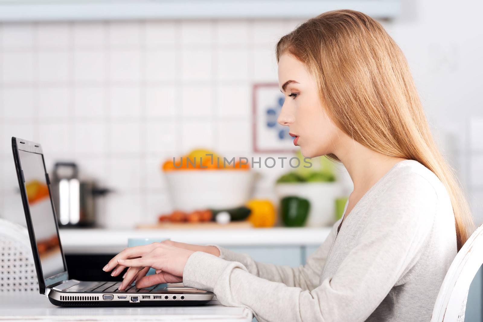 Beautiful caucasian woman working on laptop. Kitchen background.
