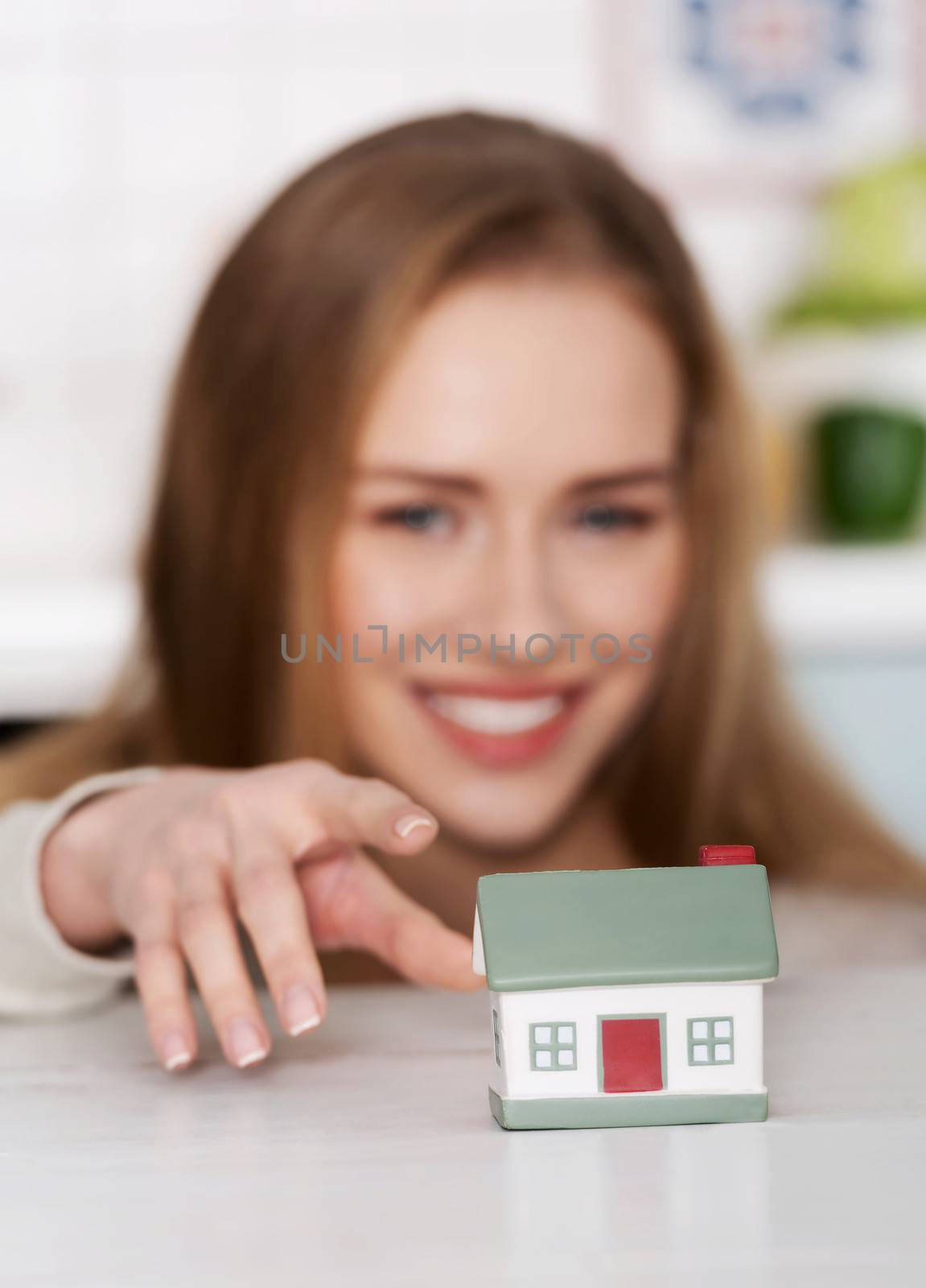 Beautiful caucasian woman and small house model. Focus on house. Indoor background.