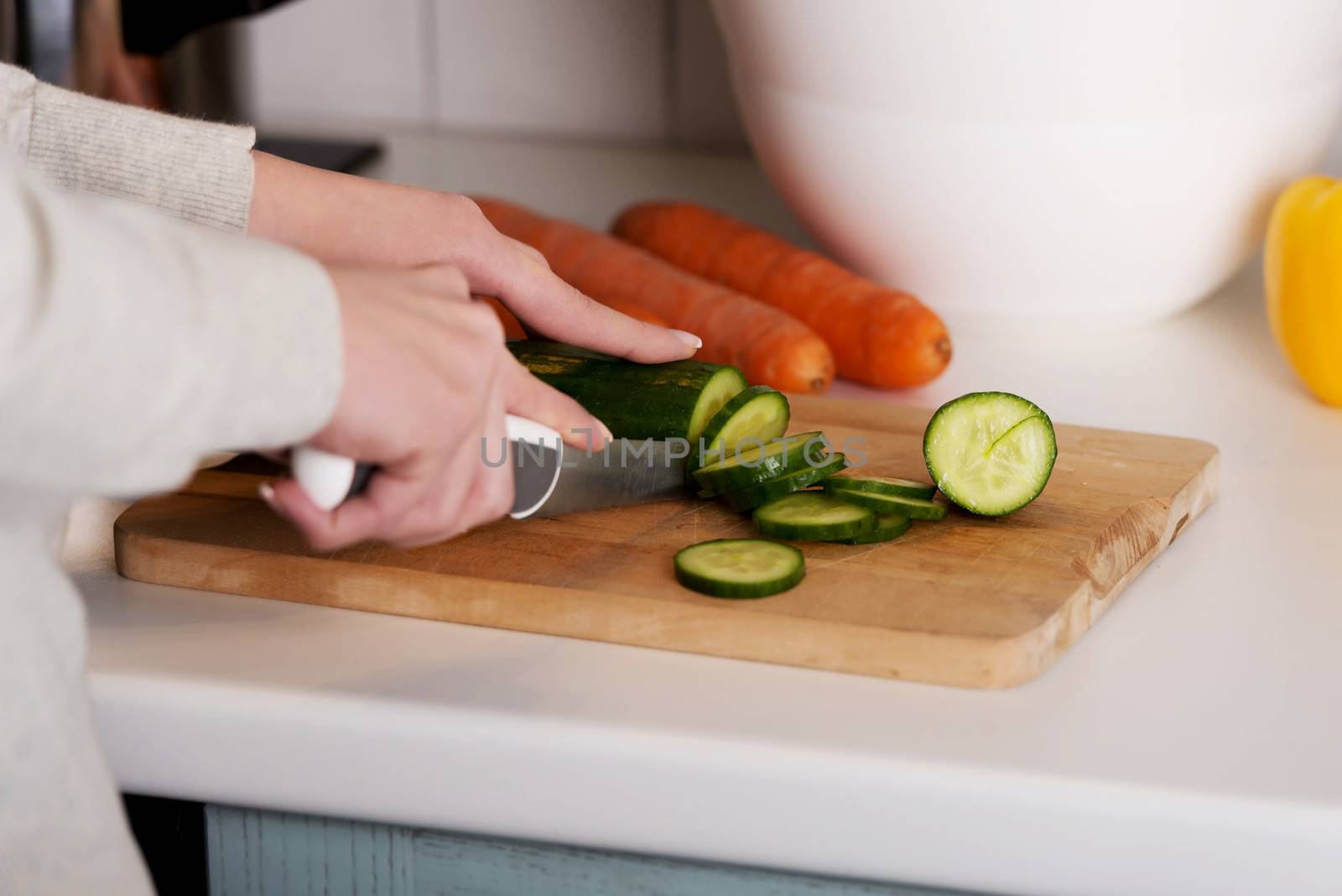 Beautiful woman in cutting cucumber on kitchen board. by BDS