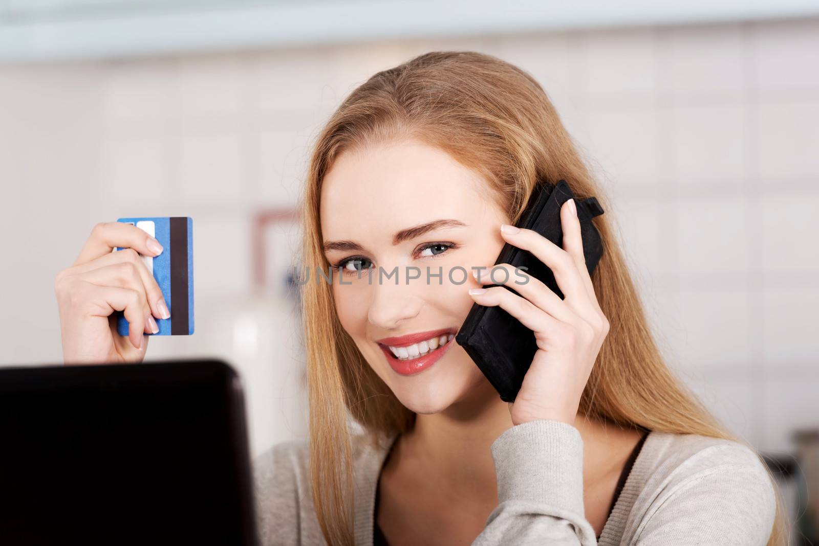 Beautiful caucasian woman doing online shopping. She's holding credit card and phone.