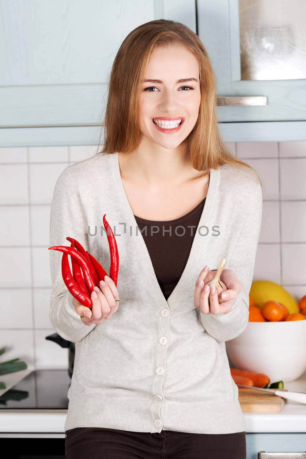 Beautiful caucasian woman is holding chili peppers and garlic. Kitchen background.