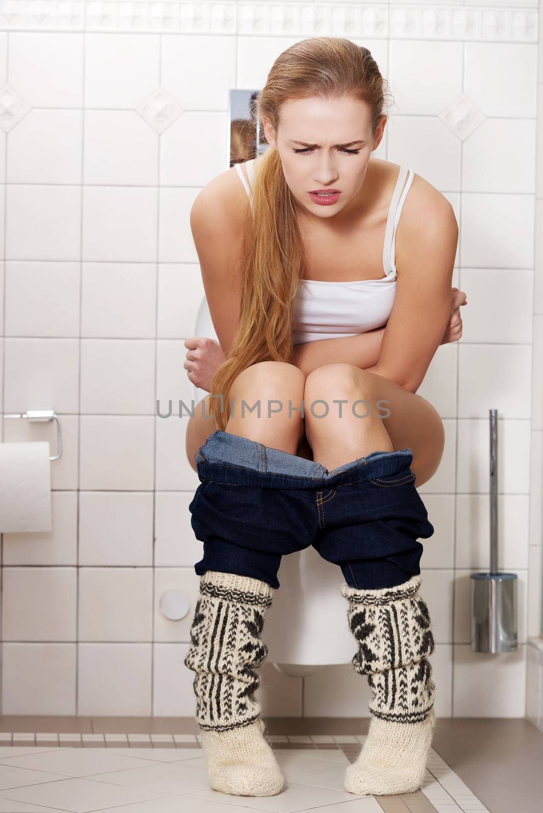 Young caucasian woman is sitting on the toilet. urinary bladder problem or pregnancy or sickness concept.