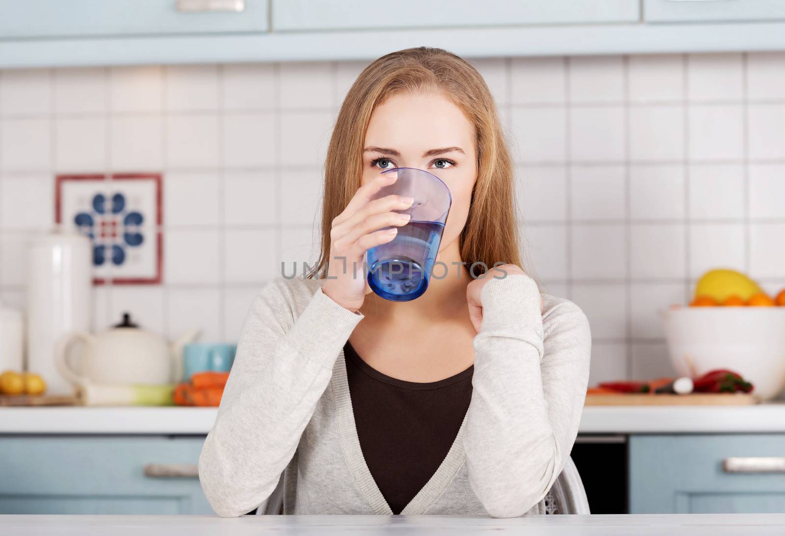 Beautiful caucasian woman sitting in the kitchen and drinking fresh water.