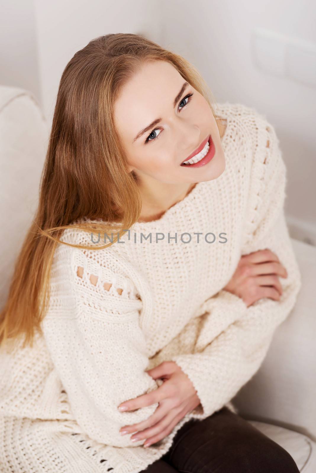 Beautiful woman in bright sweater sitting on a couch and smiling.