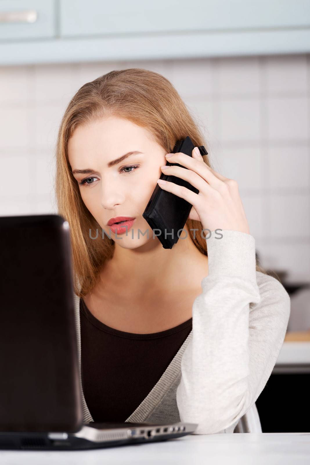 Beautiful caucasian woman talking through phone and working with laptop. Indoor background.