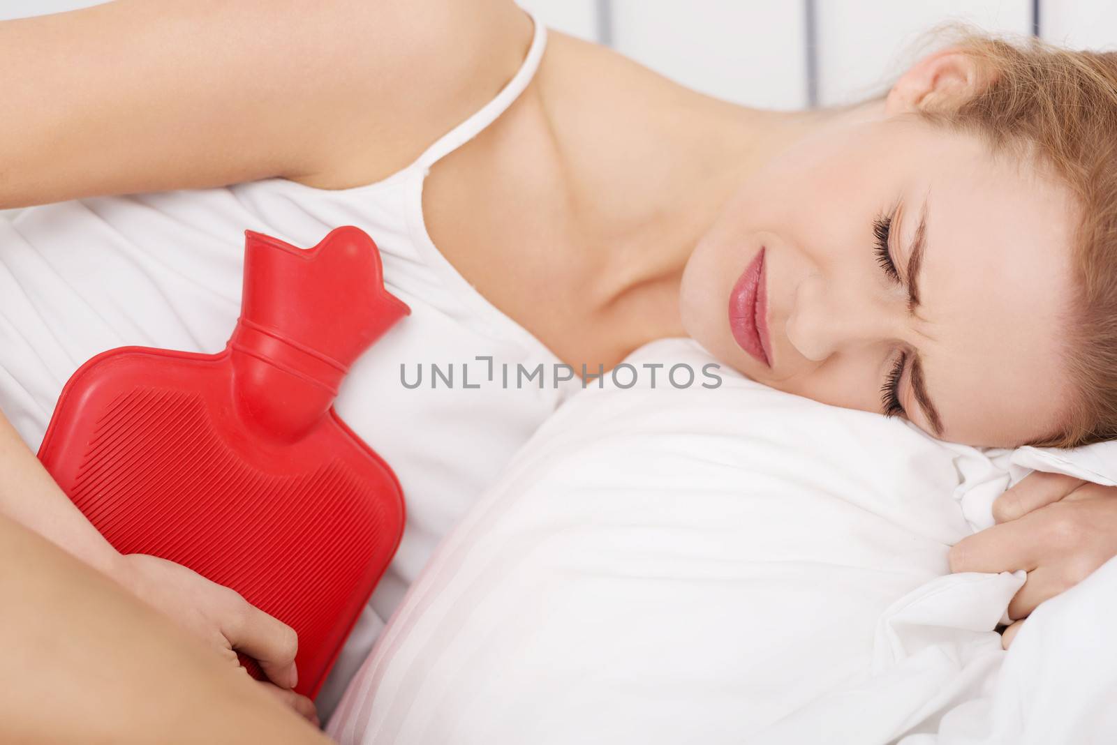 Beautiful caucasian woman lying in bed with hot water bag and holding it on her belly.