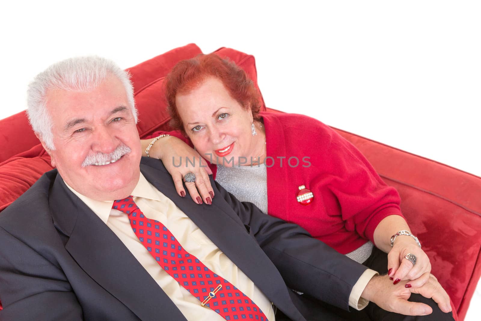 Senior couple sitting on a comfortable red couch by coskun