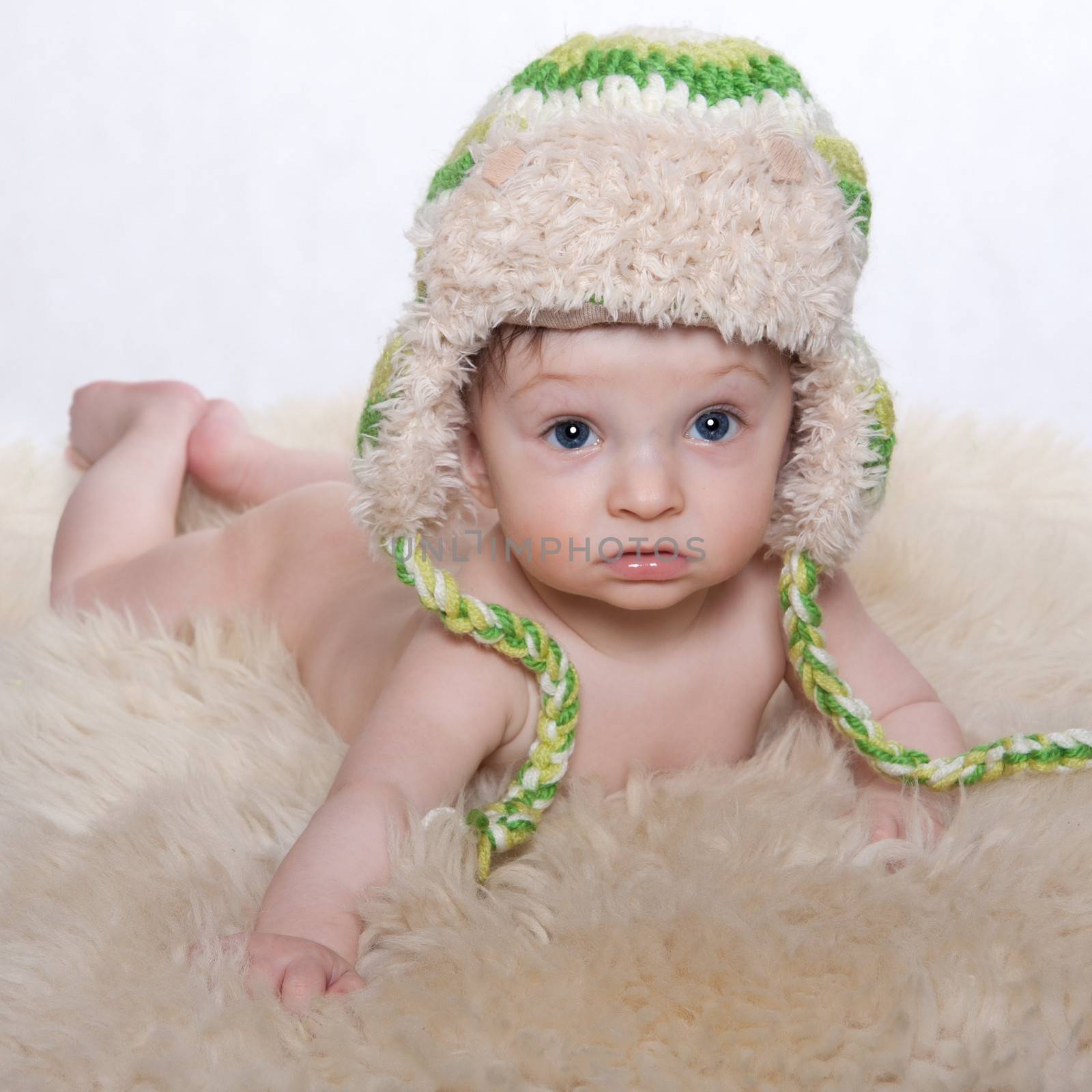 Little baby boy, lying naked on stomach on woolen fleece, on his head is cap, on a white background