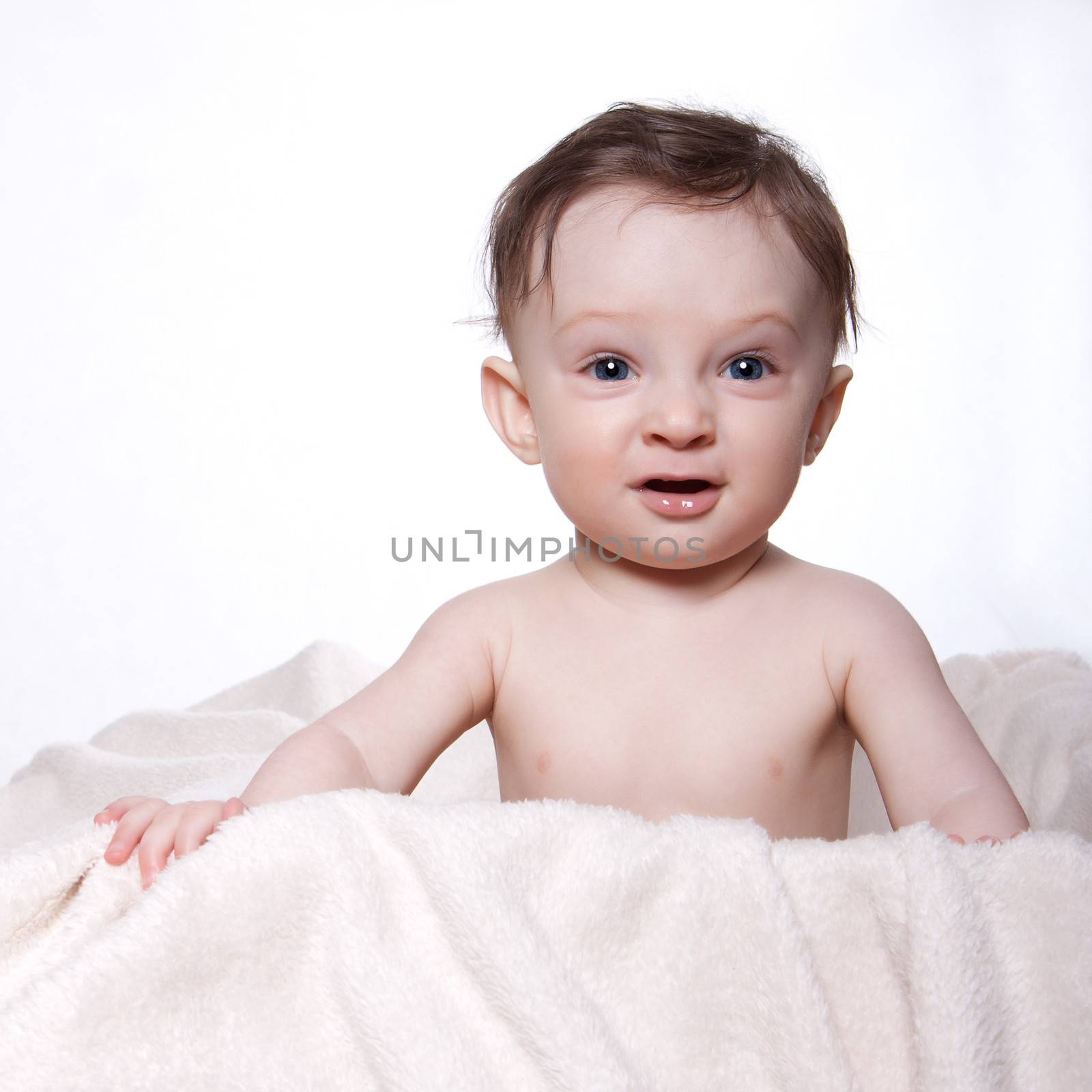 Little baby boy sitting naked on a blanket, in a box, on a white background