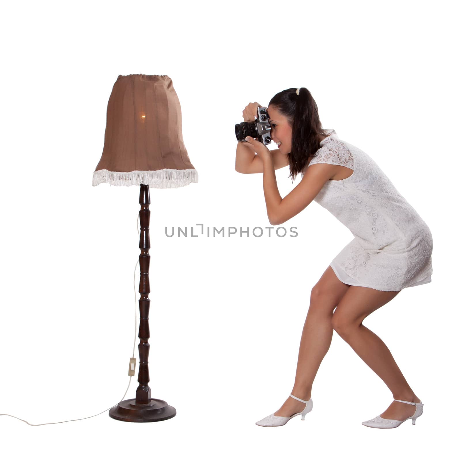 Retro woman in white dress, standing next to the old lamp and take pictures, with old camera isolated on white background