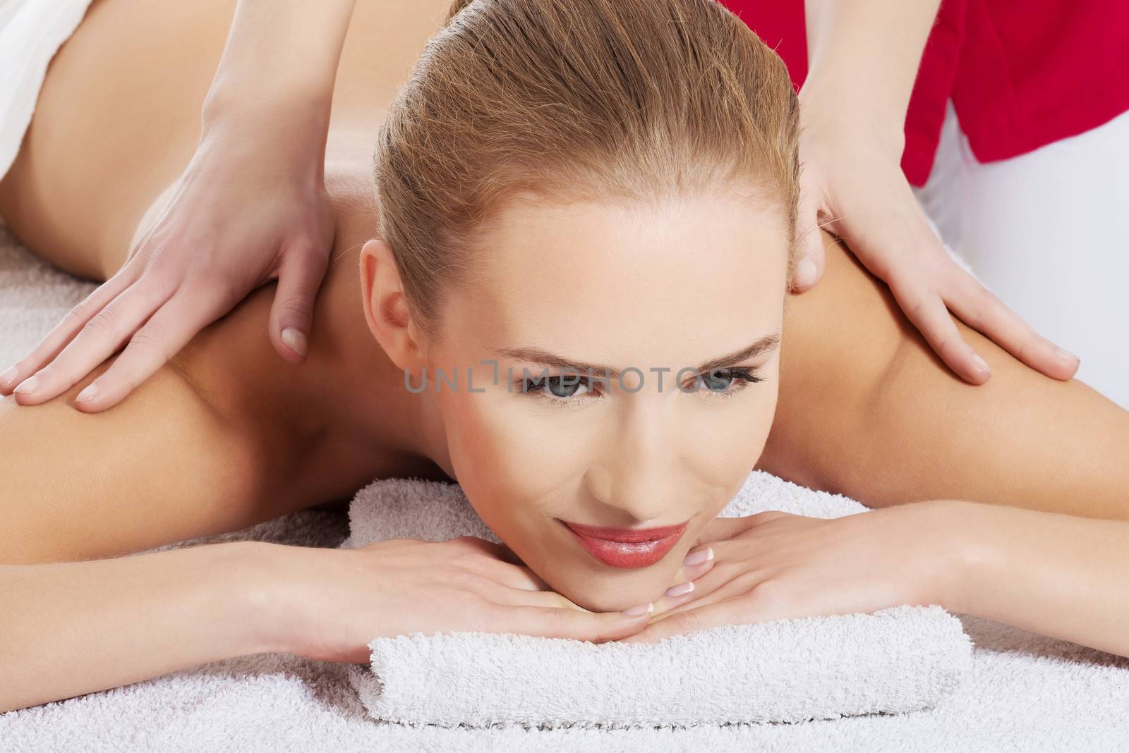 Beautiful young caucasian woman lying on a massage table and being massaged, relaxing. Spa concept.