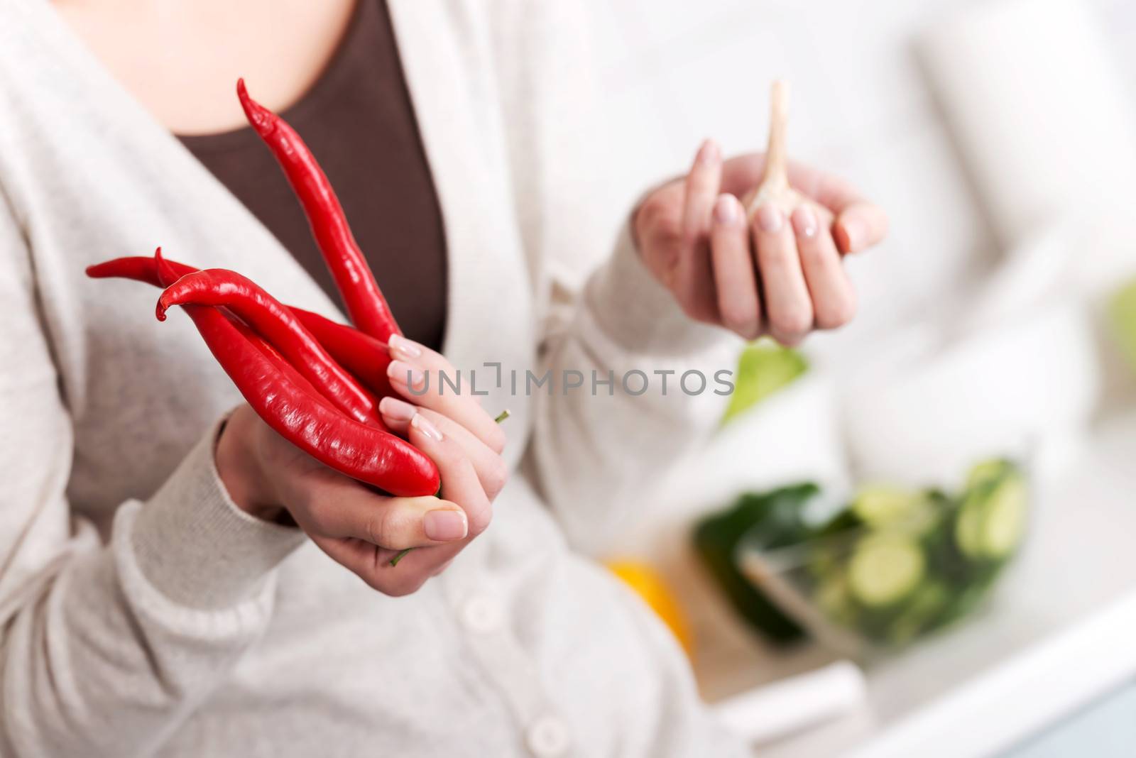 Beautiful caucasian woman is holding chili peppers and garlic. Kitchen background.