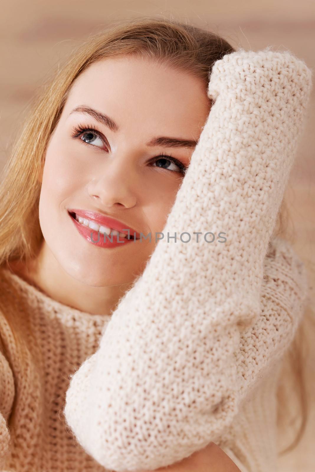 Beautiful caucasian woman is sitting on wooden floor and wearing bright sweater.