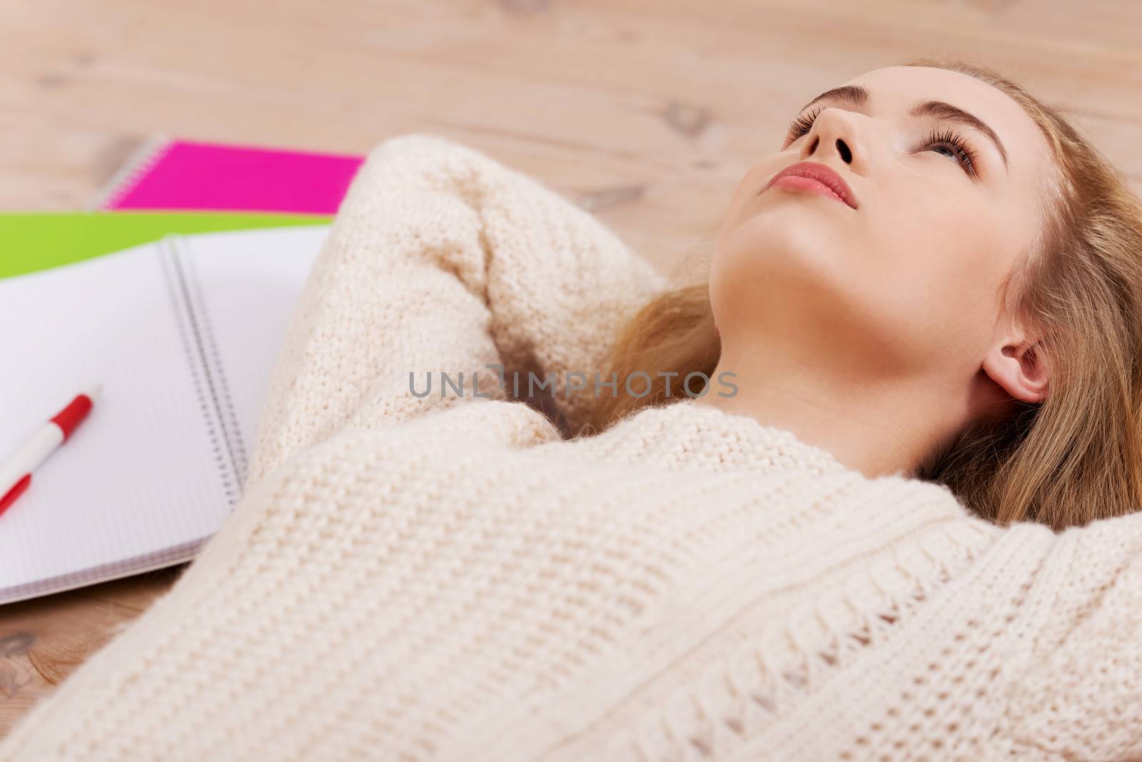 Young beautiful student woman is lying on the wooden floor around books.