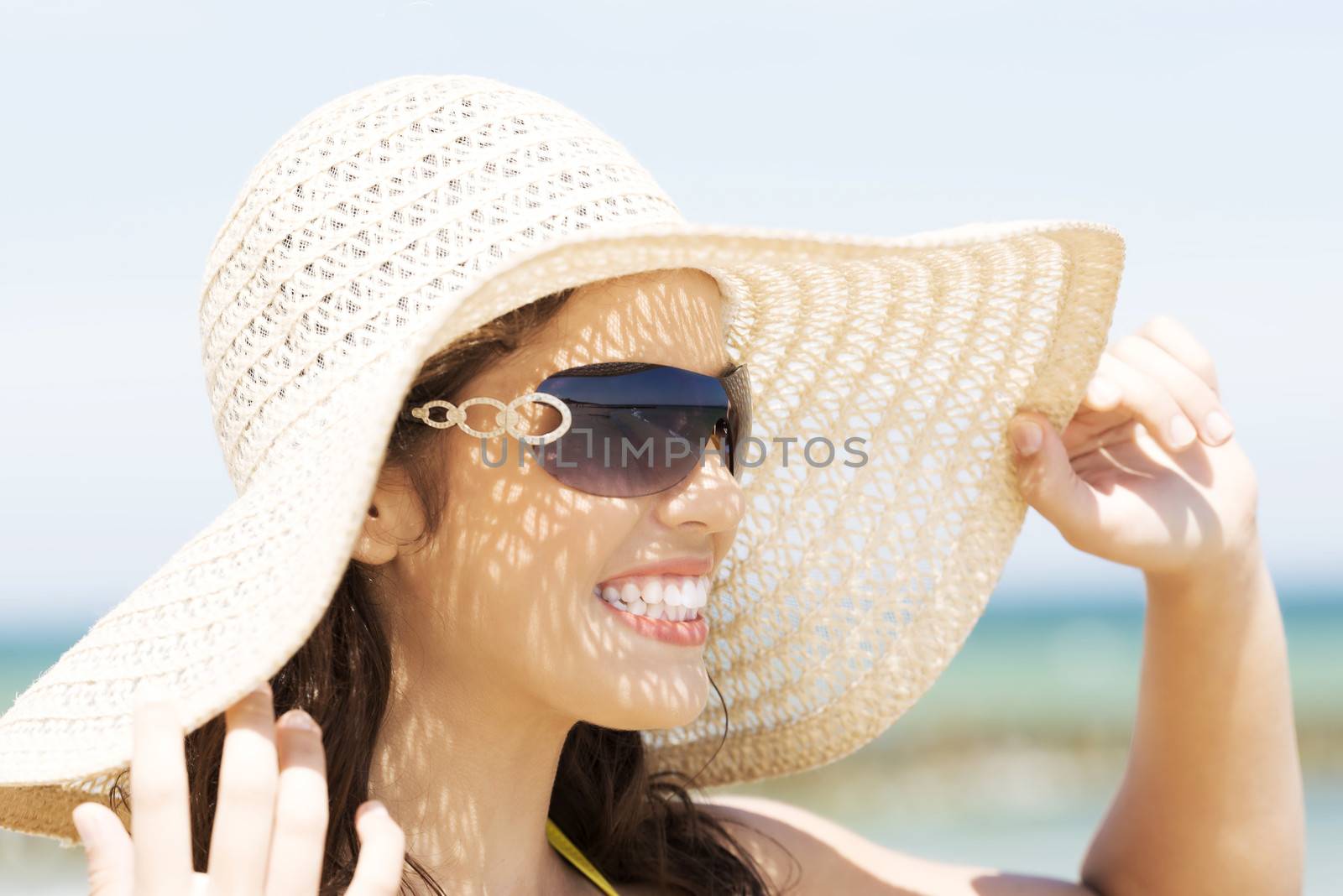 Beautiful young woman in a hat and swimsuit over seaside sunny day background.