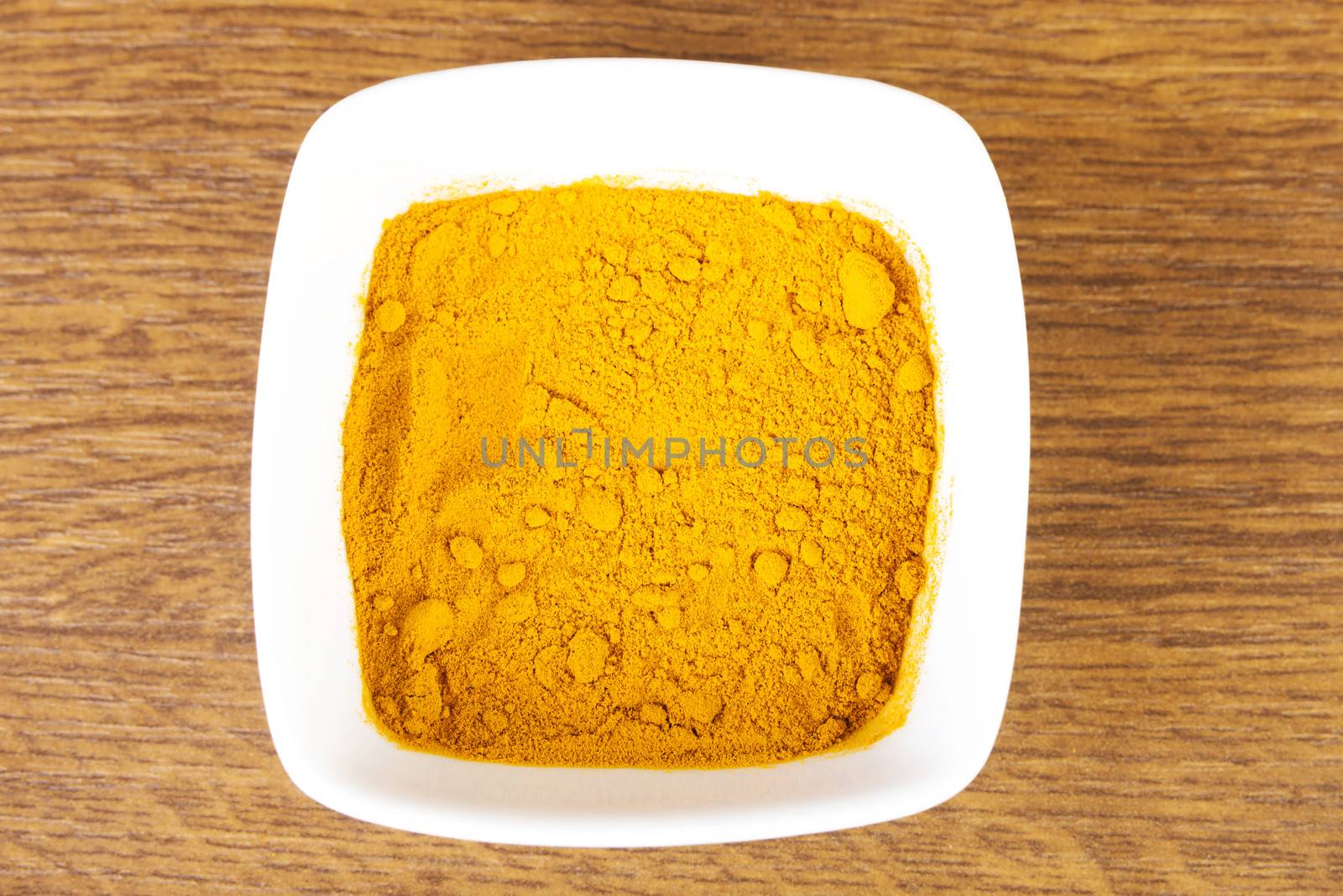 Curcuma, curry, yellow- orange spice in a bowl. Over wooden background.