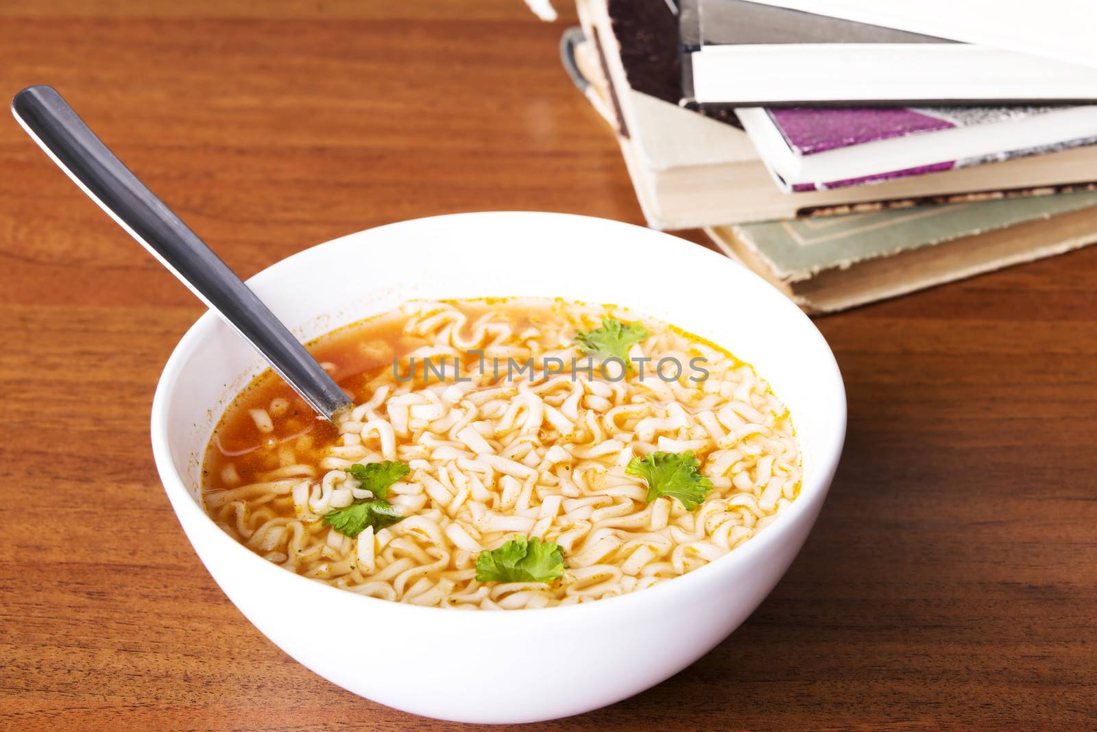 Chinese, vegetable, pasta soup next to books. On wooden table.