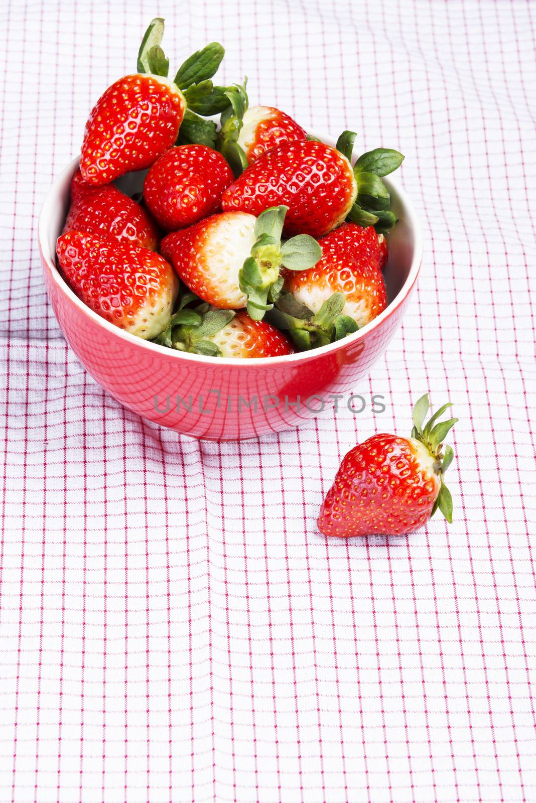Fresh red strawberries in a bowl. Over kitches clothes background.