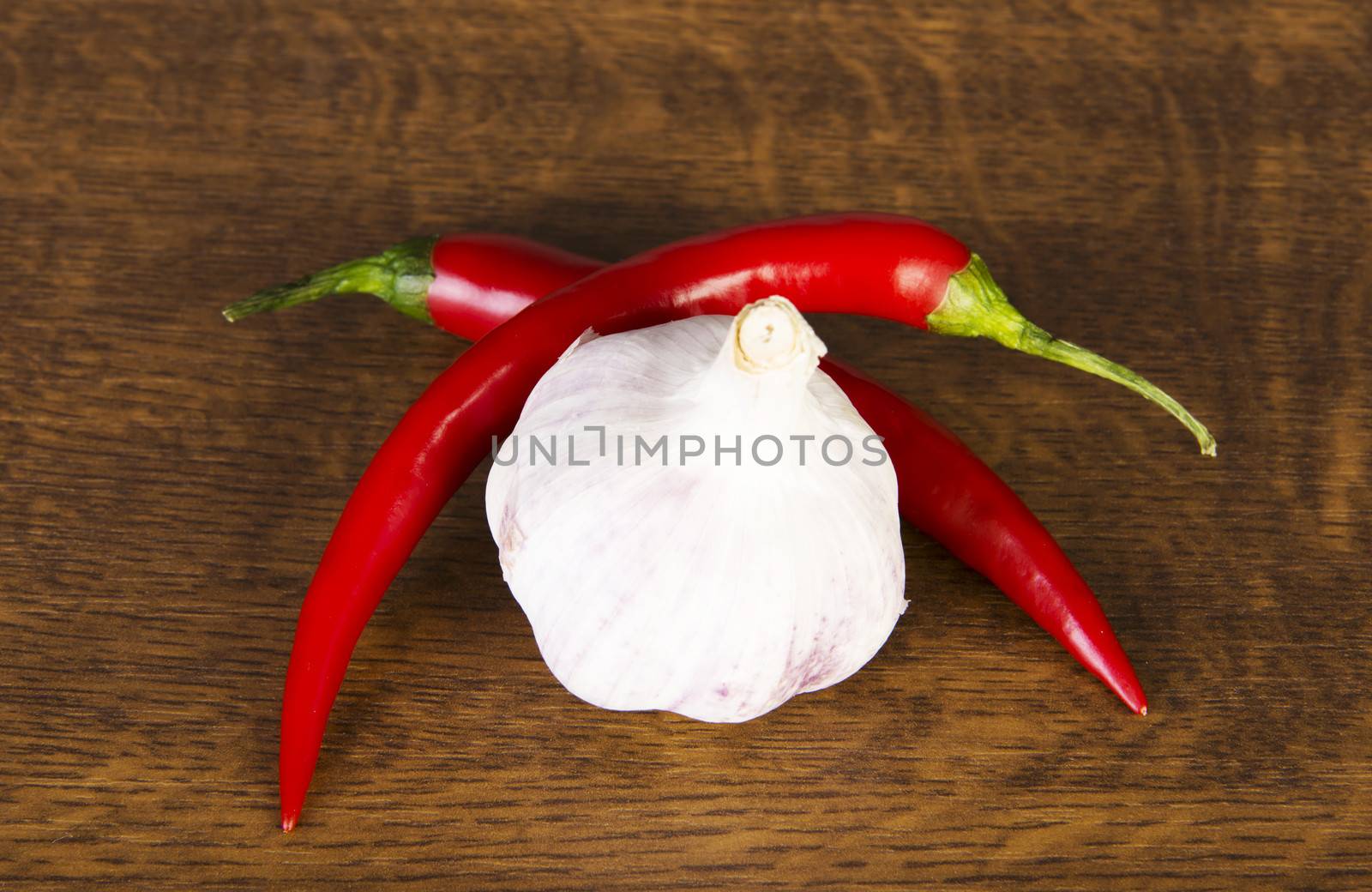 Two chili peppers lying with garlic over wooden background.