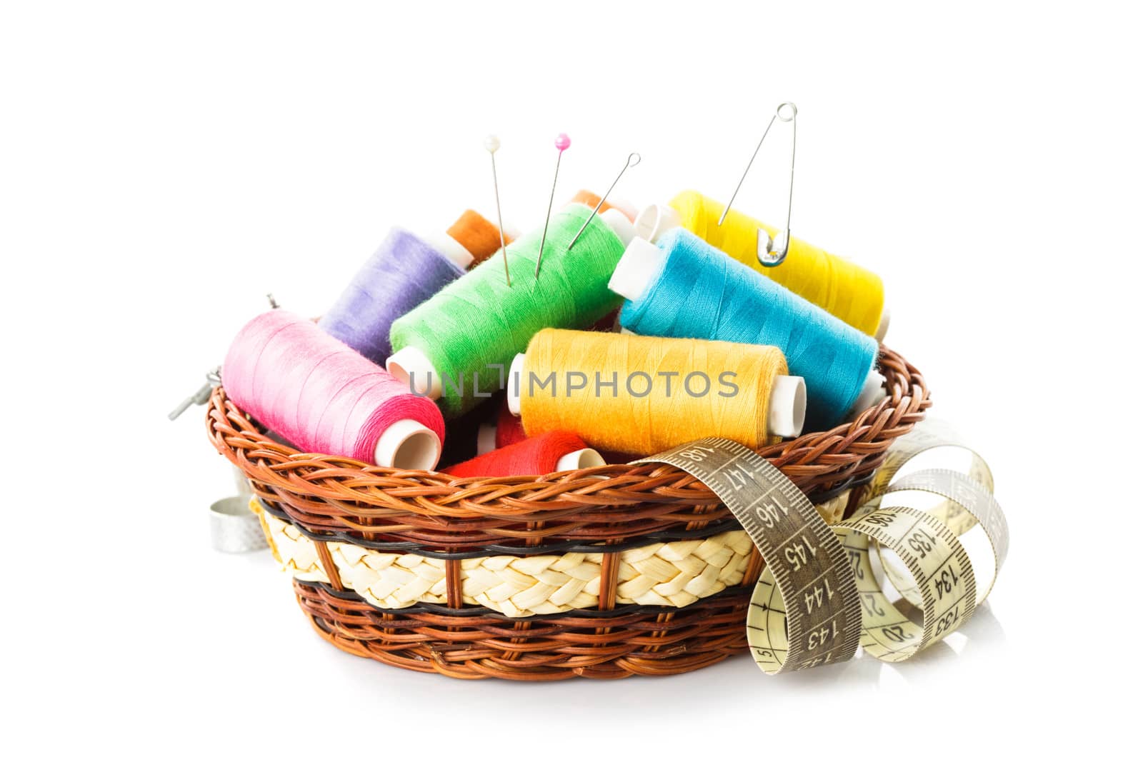 Sewing items in basket: threads, pins, meter and scissors on white