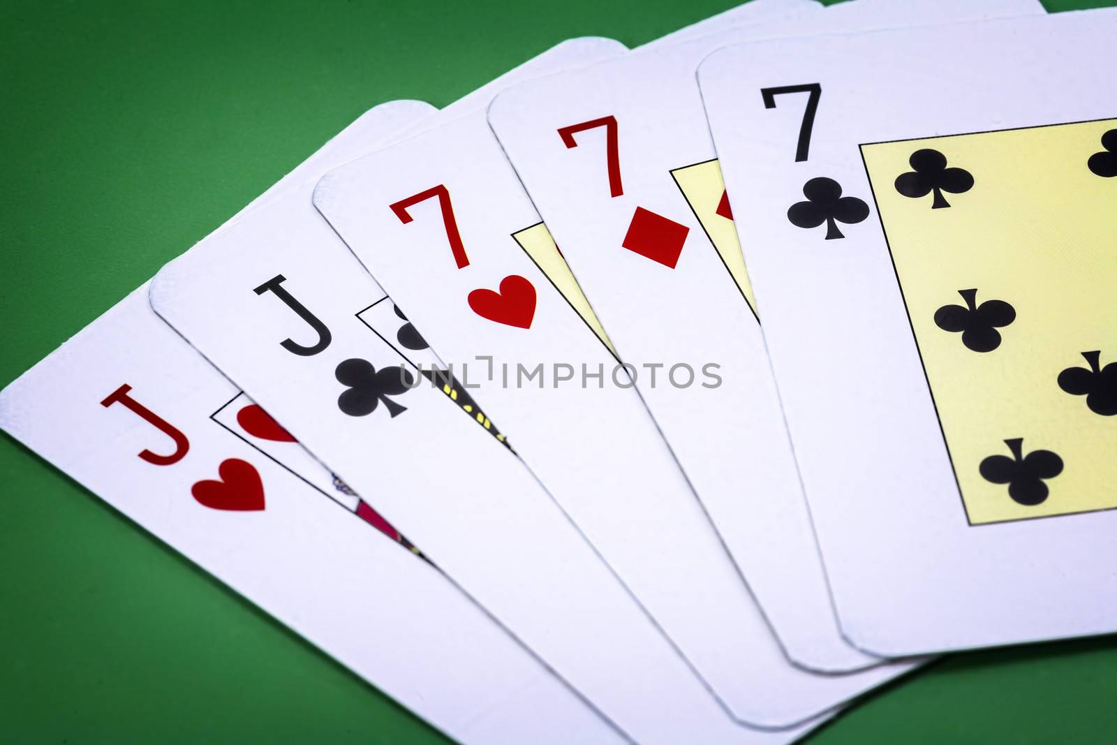 Poker hand call full house, composed by couple of j and three letters of the number seven on green background