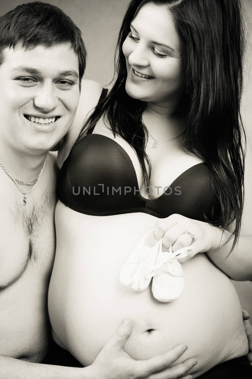 pregnant woman with a child's shoe, her husband tenderly holding her tummy, black and white