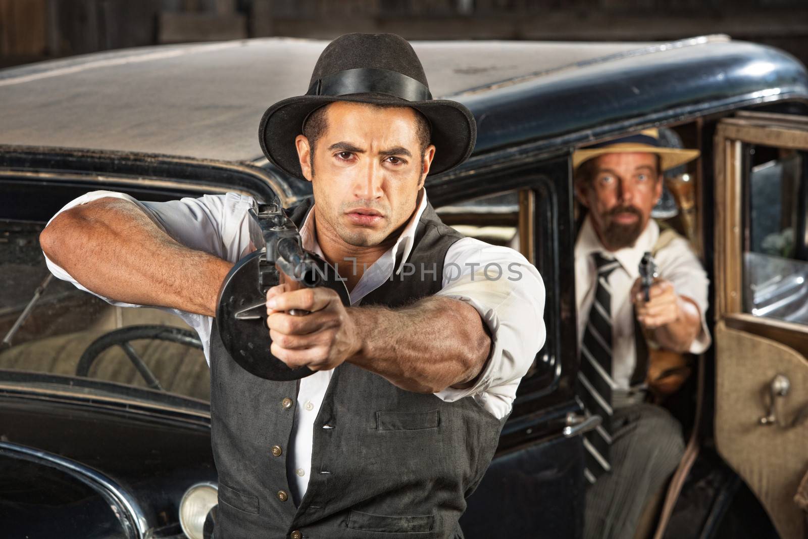 Tough 1920s vintage gangsters by car with weapons