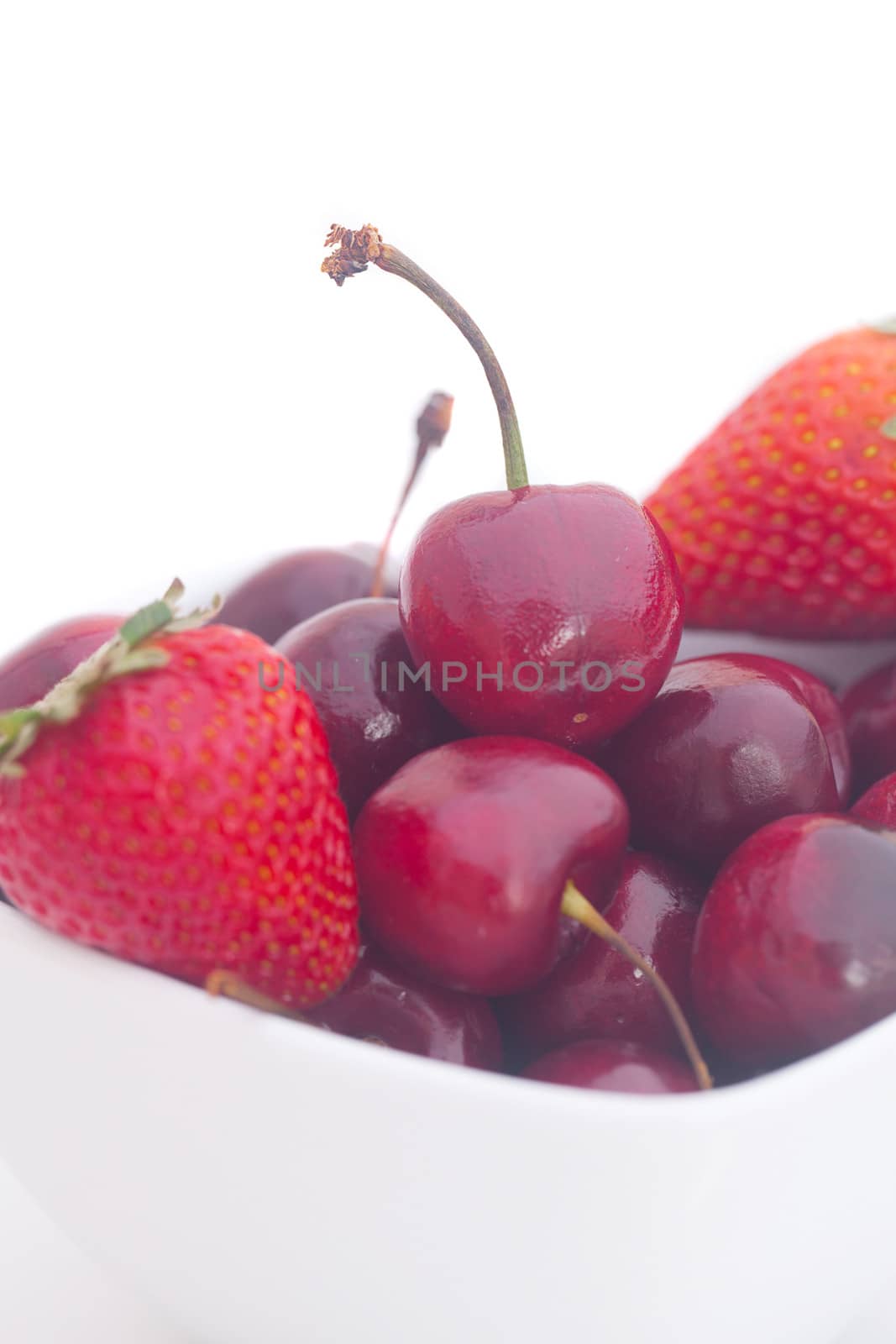 Cherries and strawberry in a ceramic bowl isolated on white by jannyjus