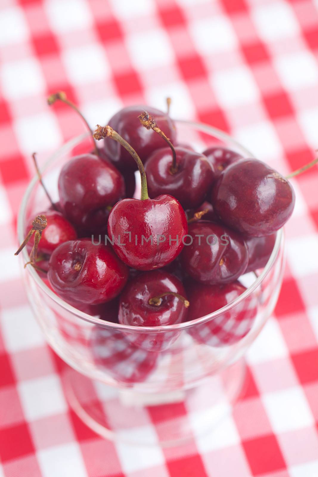 Cherries in a glass bowl on checkered fabric by jannyjus