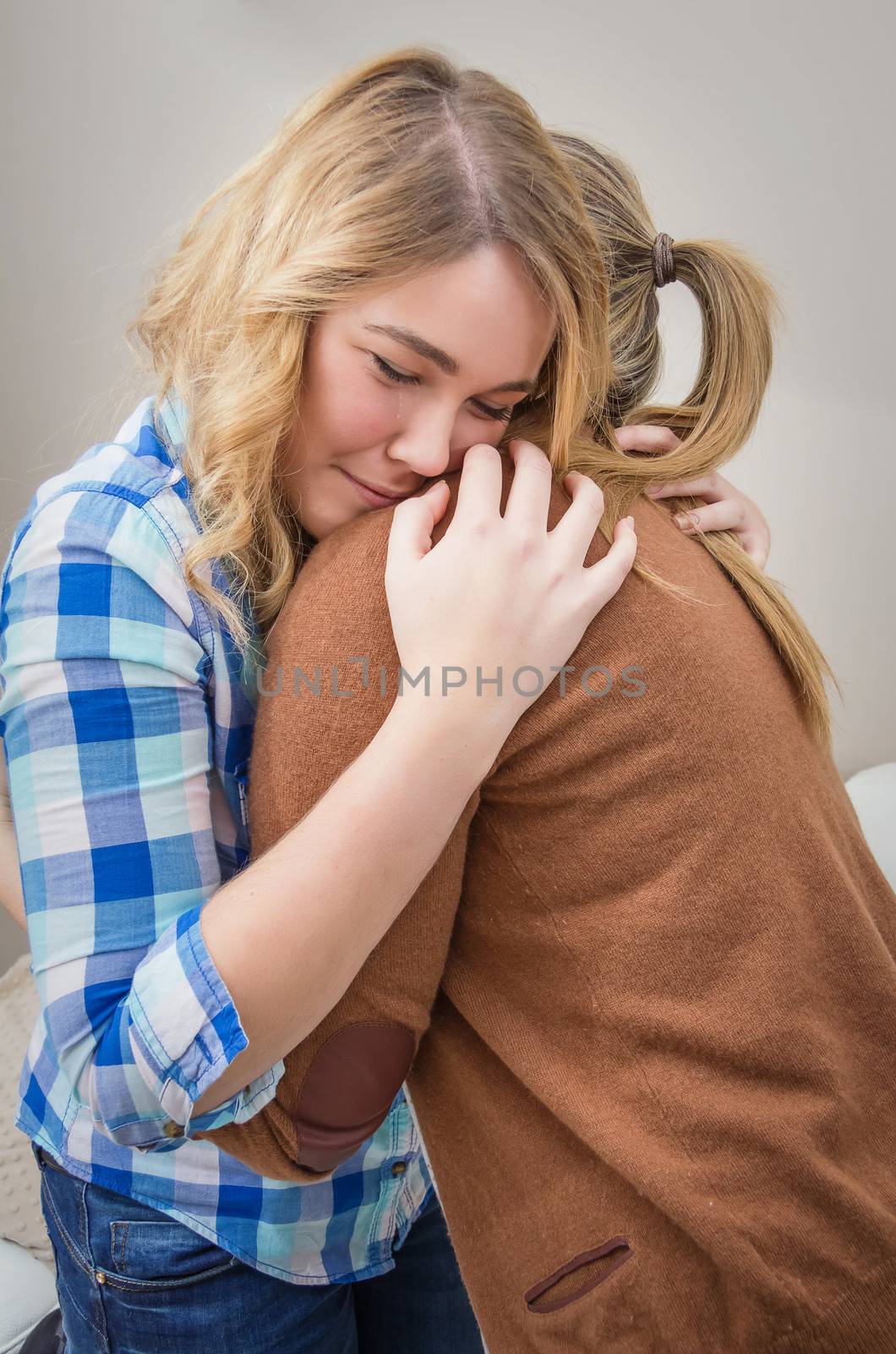 Closeup on sad teen daughter crying by problems in the shoulder of her mother. Mother embracing and consoling daughter.
