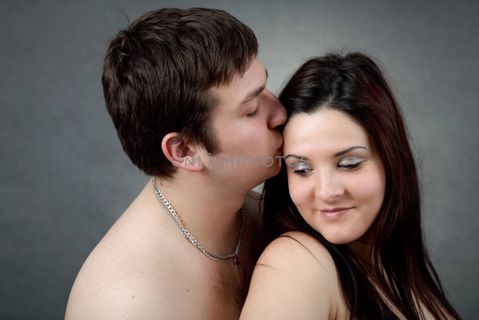 portrait of beautiful young couple on grey background, man kissing woman