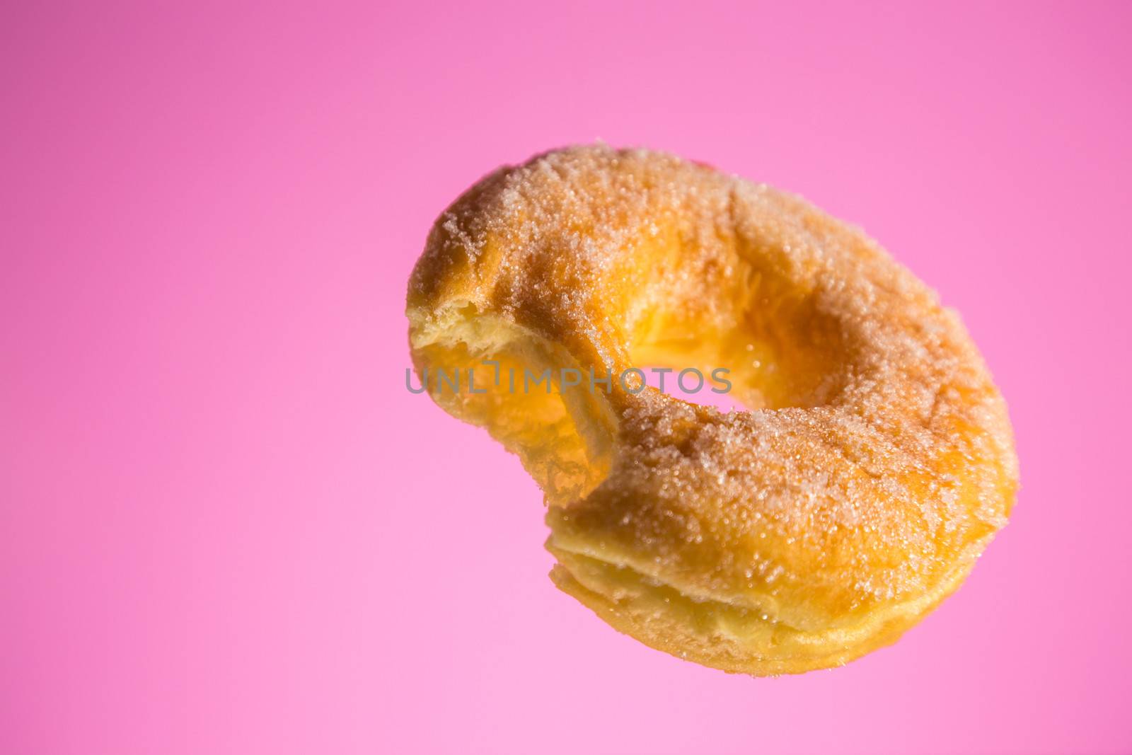 Bitten sugar coated donut, studio shot on light pink background 