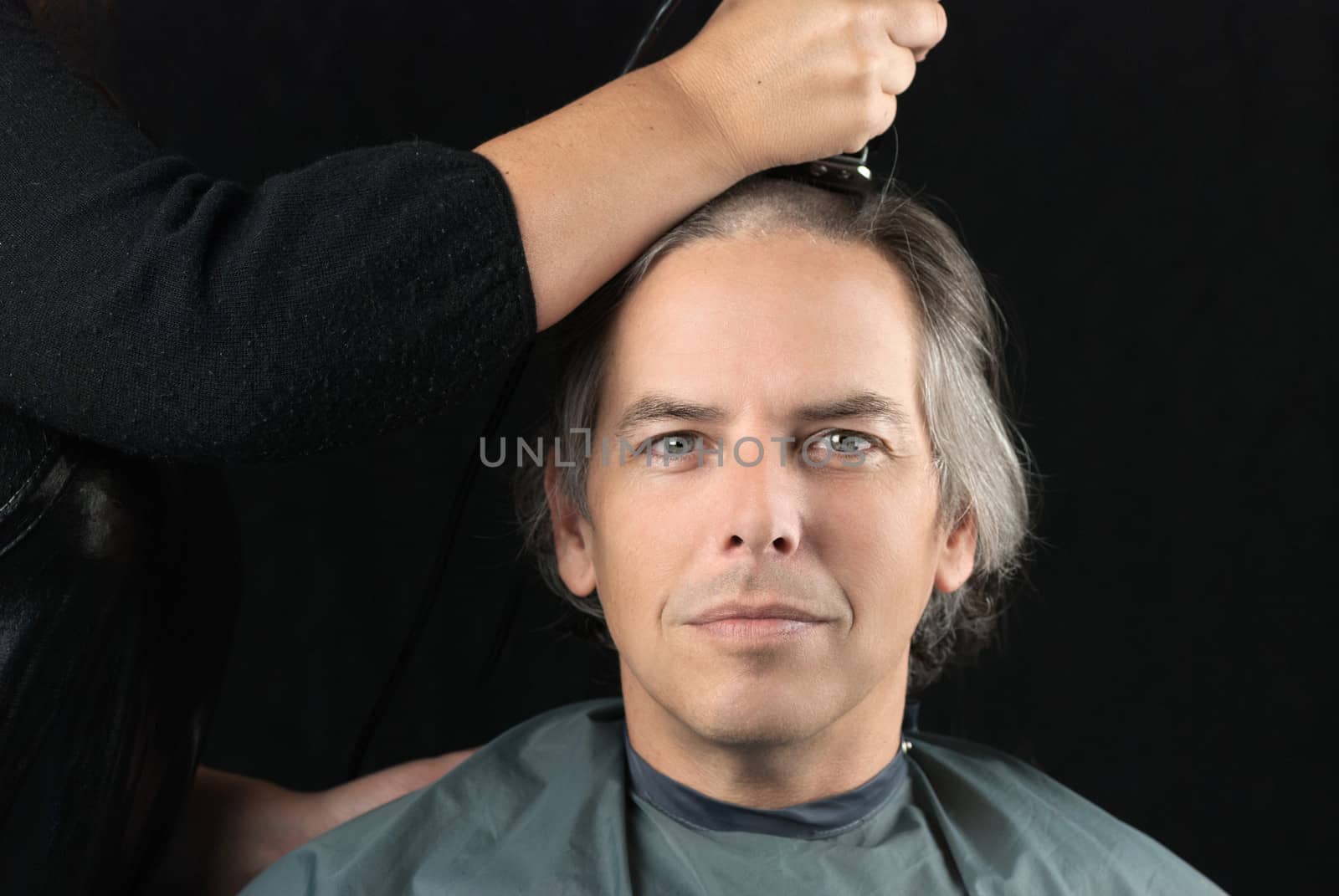 Close-up of a serious man looking to camera while his long hair is shaved off for a cancer fundraiser.