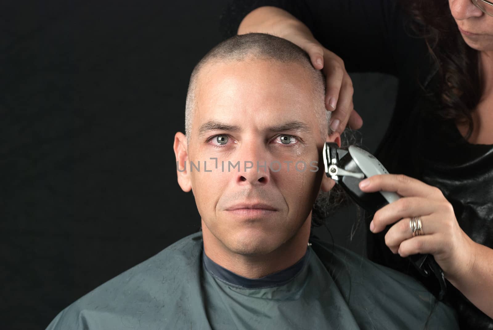 Close-up of a mourning man getting his head shaved. Looking to camera,