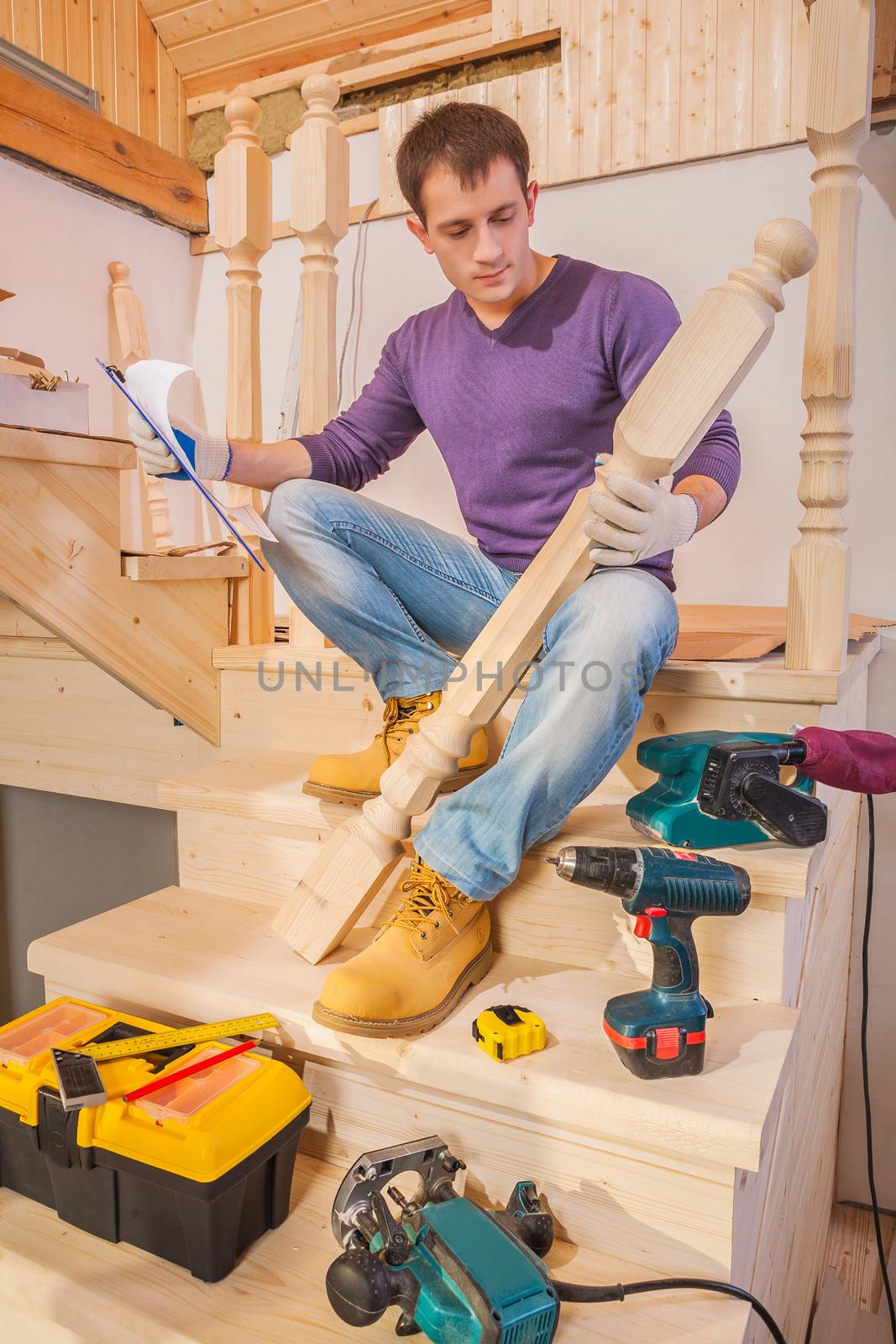 a young construction worker holding post of ladder and blueprint