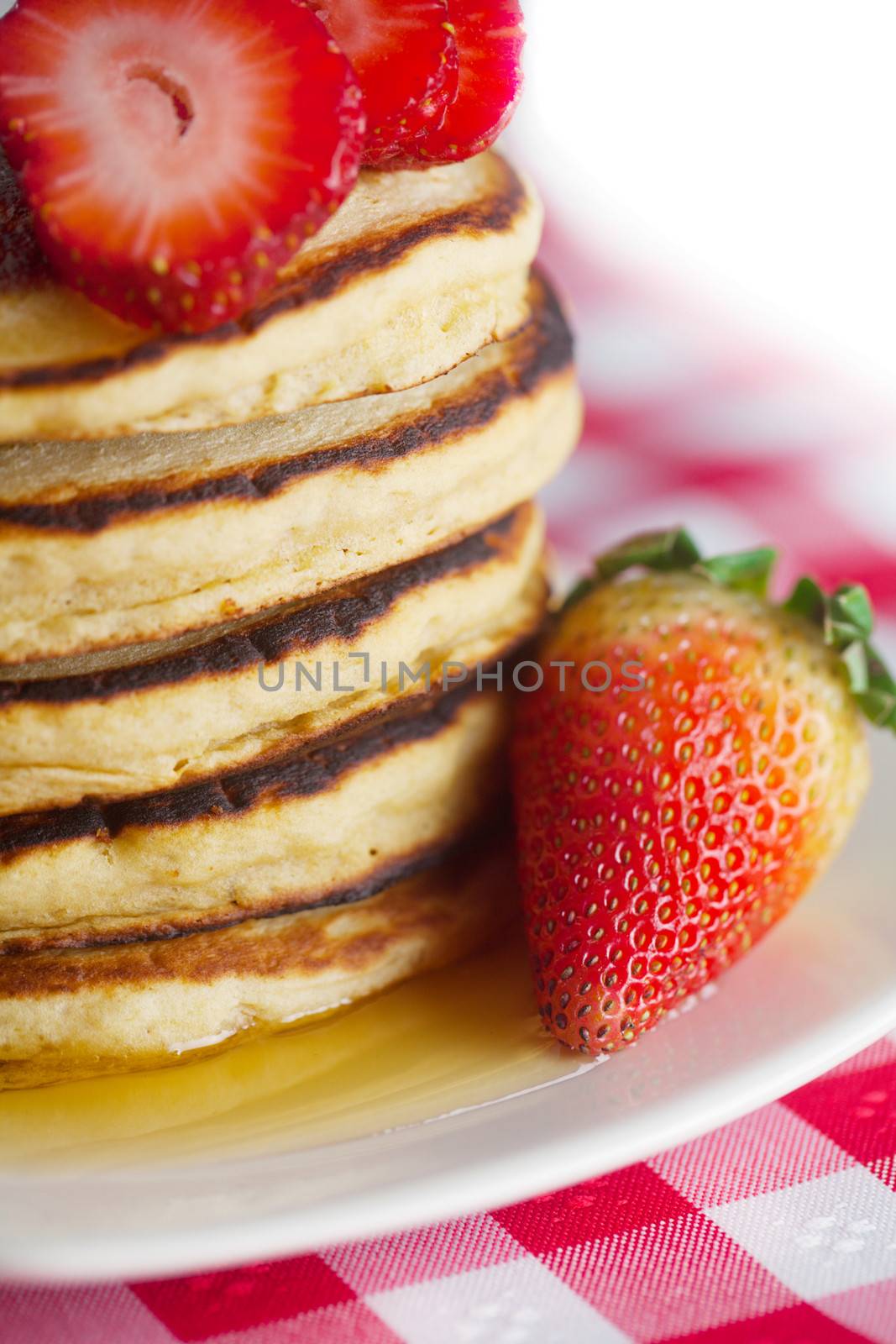 Pancakes, honey and strawberry on checkered fabric