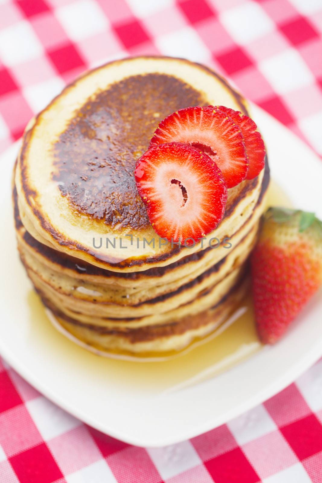 Pancakes, honey and strawberry on checkered fabric