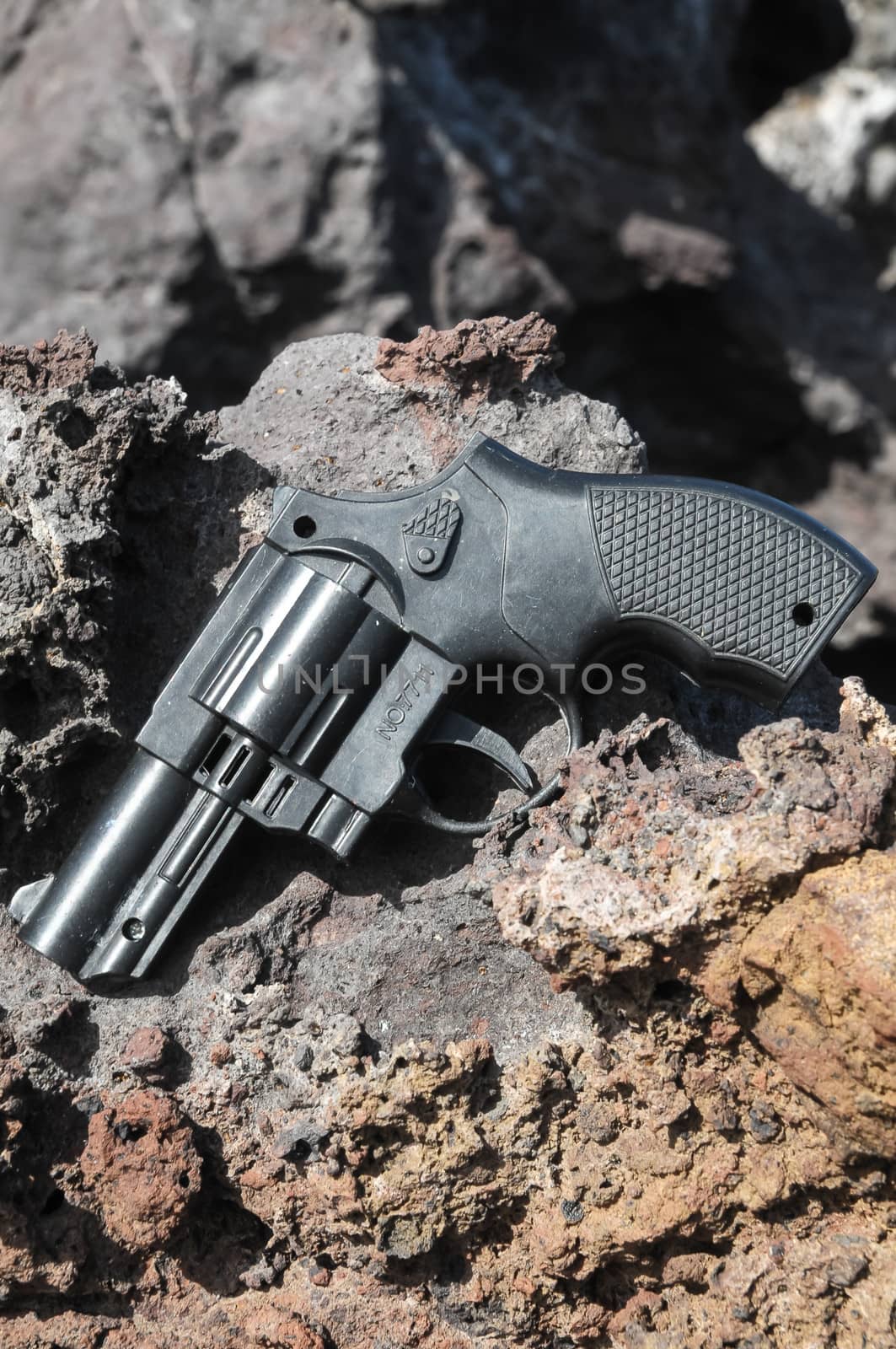 Plastic Revolver Gun Toy on the Volcanic Rocks