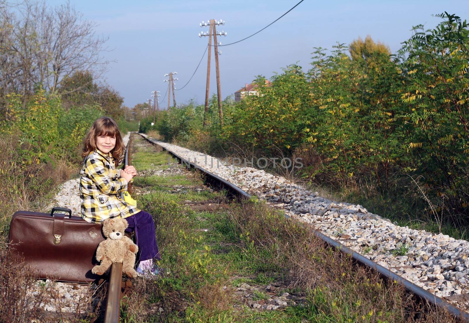 little girl sitting on suitcase and waiting for train by goce