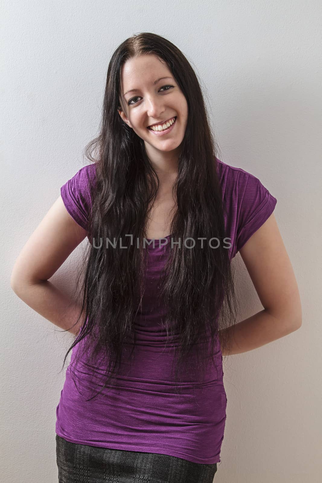 young woman with long black hair and a purple shirt, leaning on a wall with her hand on her back