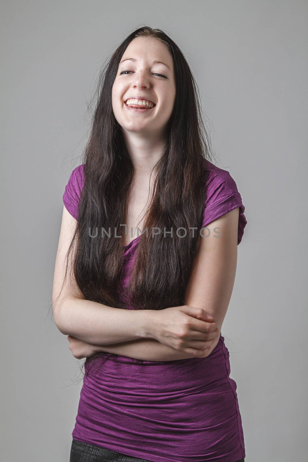 young woman with long black hair and a purple shirt laughing, holding her stomach and sticking out her tongue