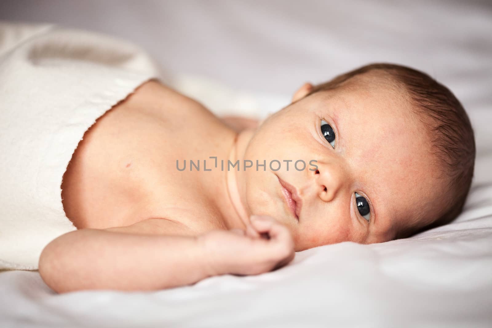 Cute newborn baby boy looking at camera in his bed