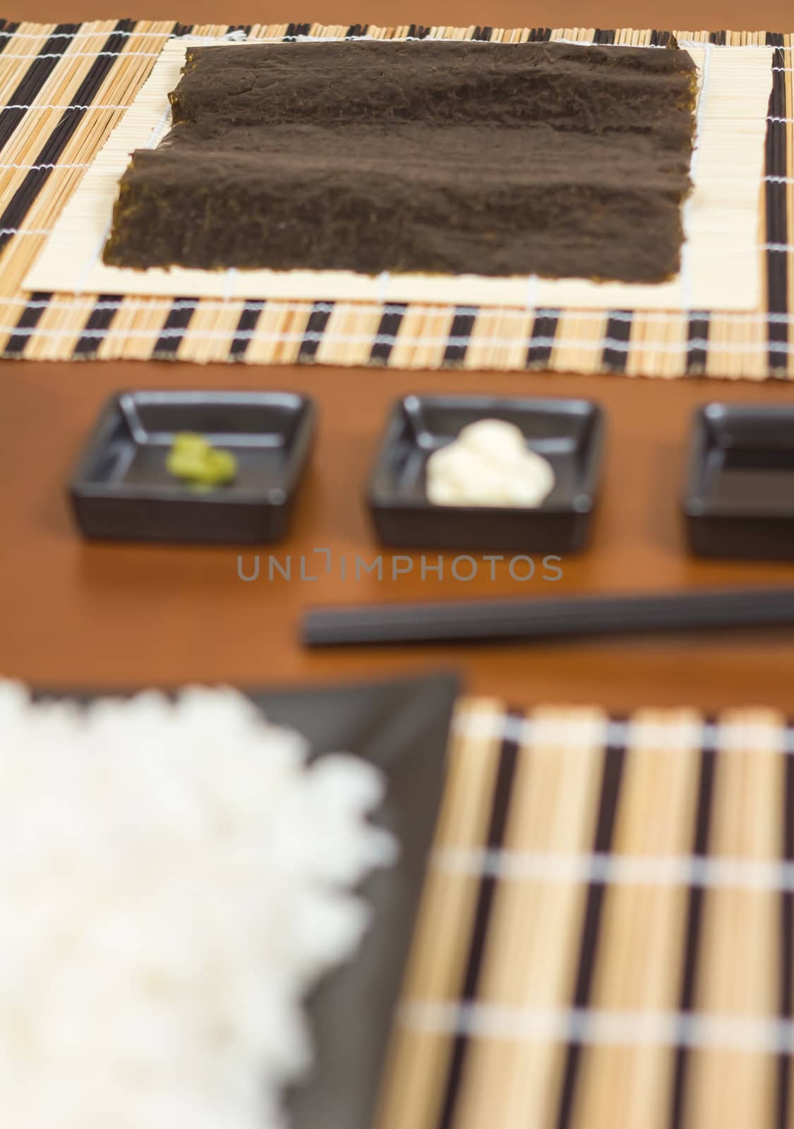 Nori seaweed sheet ready to make japanese sushi rolls, with sauces and rice in the foreground. Selective focus in nori seaweed.