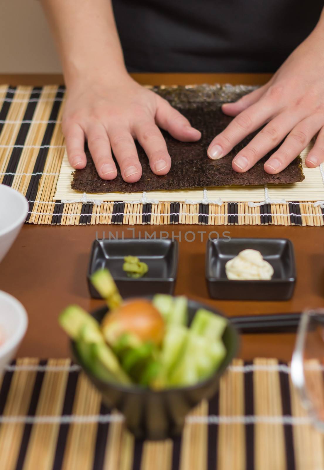 Woman chef ready to prepare japanese sushi rolls, with principal ingredients in the foreground. Selective focus in nori seaweed.