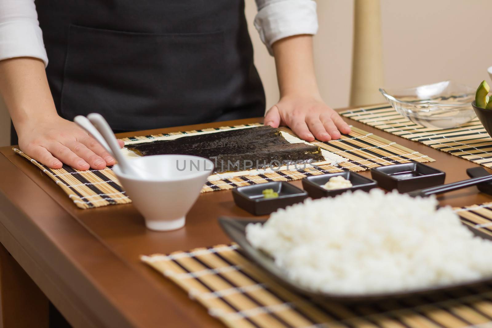 Woman chef ready to prepare japanese sushi rolls, with principal ingredients in the foreground. Selective focus in nori seaweed.