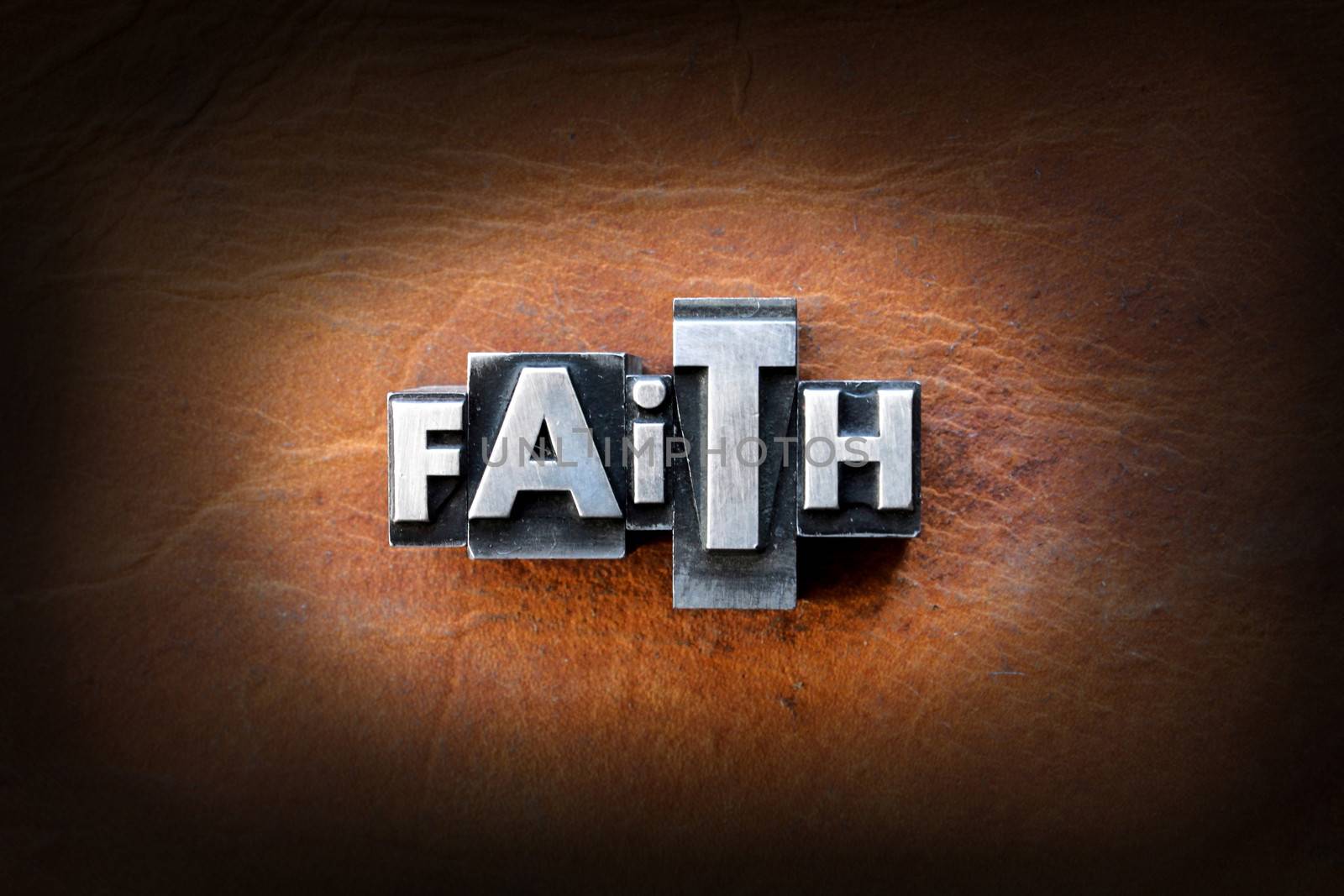 The word faith made from vintage lead letterpress type on a leather background.