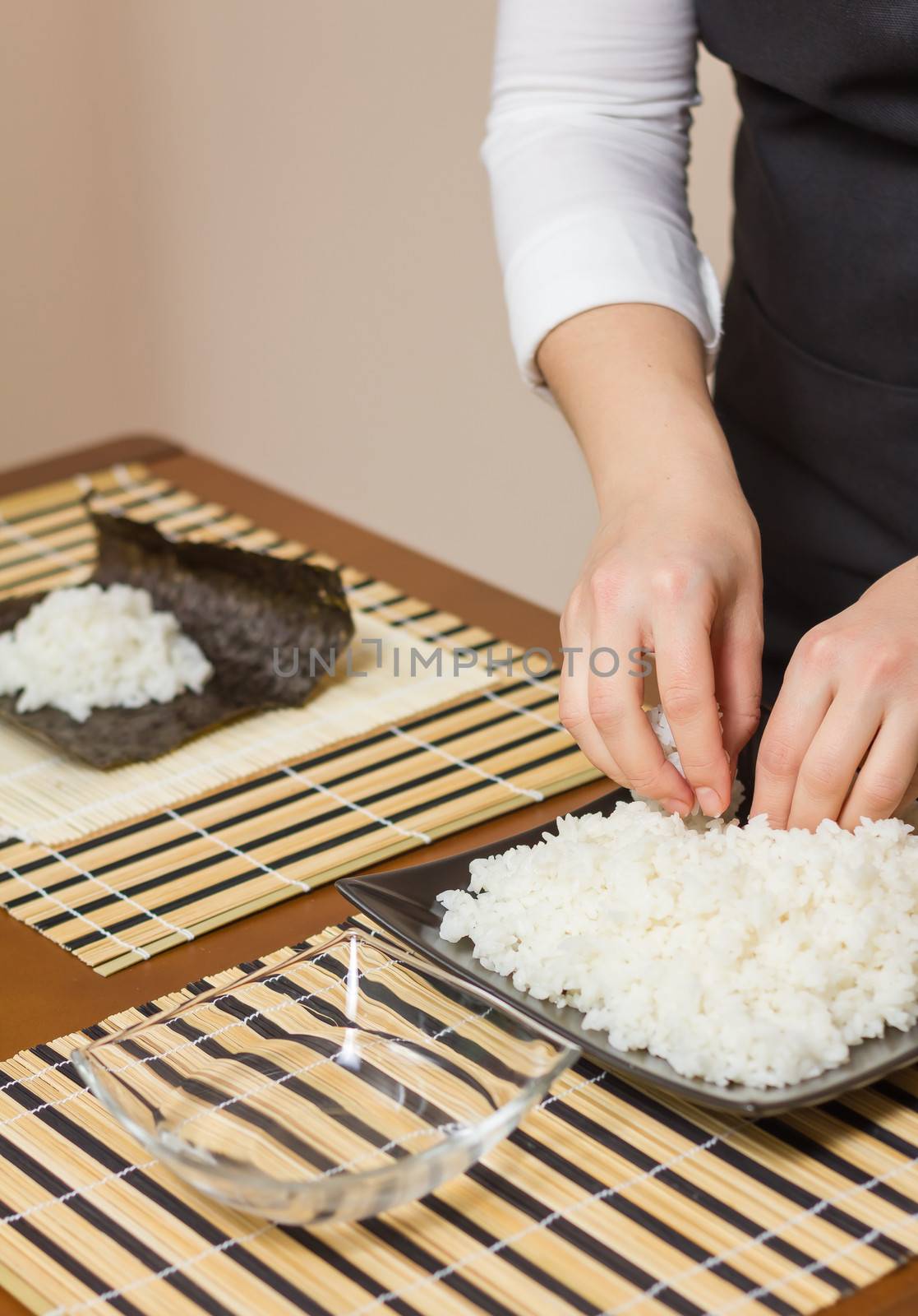Hands of woman chef filling japanese sushi rolls with rice on a nori seaweed sheet. Selective focus on rice plate.