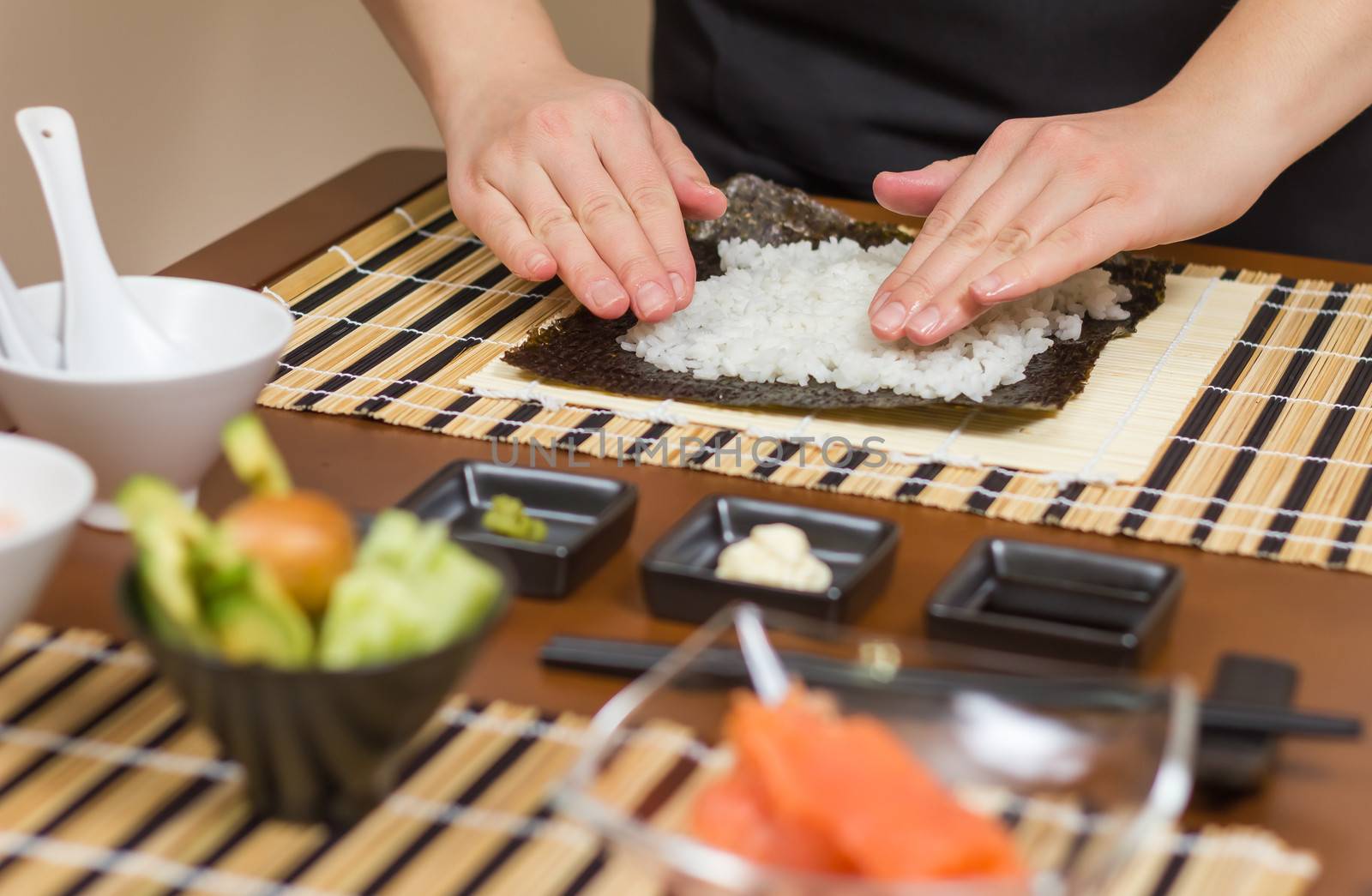 Hands of woman chef filling japanese sushi rolls with rice on a nori seaweed sheet. Selective focus in sushi roll.