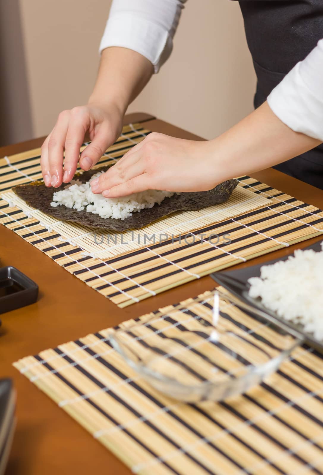 Hands of woman chef filling japanese sushi rolls with rice on a nori seaweed sheet